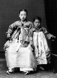 A young Korean woman poses with her daughter wearing traditional hanbok dress, c. 1910.<br/><br/>Hanbok (South Korea) or Chosŏn-ot (North Korea) is the traditional Korean dress. It is often characterized by vibrant colors and simple lines without pockets. Although the term literally means 'Korean clothing', hanbok today often refers specifically to hanbok of Joseon Dynasty and is worn as semi-formal or formal wear during traditional festivals and celebrations.<br/><br/>The modern hanbok does not exactly follow the actual style as worn in Joseon dynasty since it underwent some major changes during the 20th century.